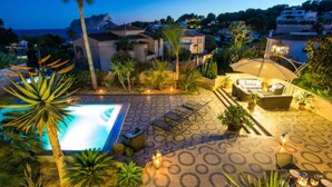 A pool area with lounge chairs and a covered seating area, surrounded by palm trees and a mountain view. - El Salvador Fustera (Benissa)