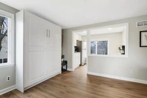 Una habitación amplia con un armario blanco grande, piso de madera y vista a un área de cocina.