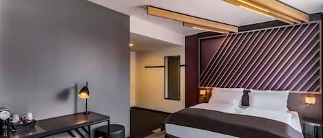 A modern hotel room with a large bed, a desk, and a chair.