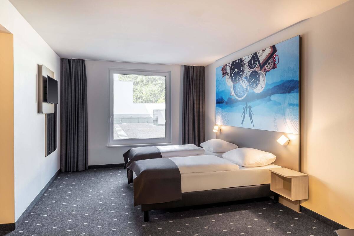 Et hotelværelse med seng, to sengeborde, fjernsyn, et vindue og et billede på væggen.