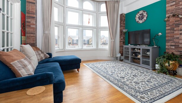 Een woonkamer met een blauwe bank, een groot raam, een televisie en een decoratieve klok aan de muur.