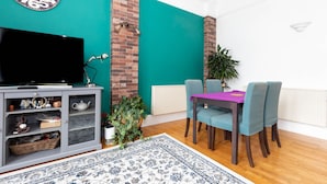 Een woonkamer met teal muren, een schouw van baksteen, een flatscreen televisie, een eettafel met stoelen en een kamerkleed met een patroon.