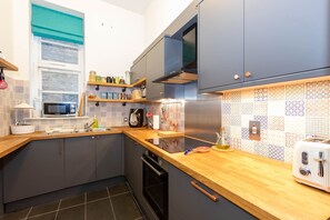 Een moderne keuken met grijze kastjes, een houten aanrecht, een magnetron, een broodrooster en een decoratieve spatwand.