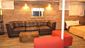 A room with a brick wall, a brown leather sofa, a wooden chest, and a red armchair. - WALKOUT BASEMENT NEAR downtown  Littleton Ave NEWARK NJ (Newark)
