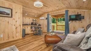 A cozy cabin interior with wooden walls, a dining area, a sofa, and a TV mounted on the wall.