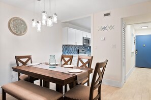 A dining area with a wooden table, four chairs, and a clock on the wall. - Xanadu 2 bedroom condo w/ Pool, Tennis walk to Beach, Coligny Celebration Park! (Hilton Head Island)
