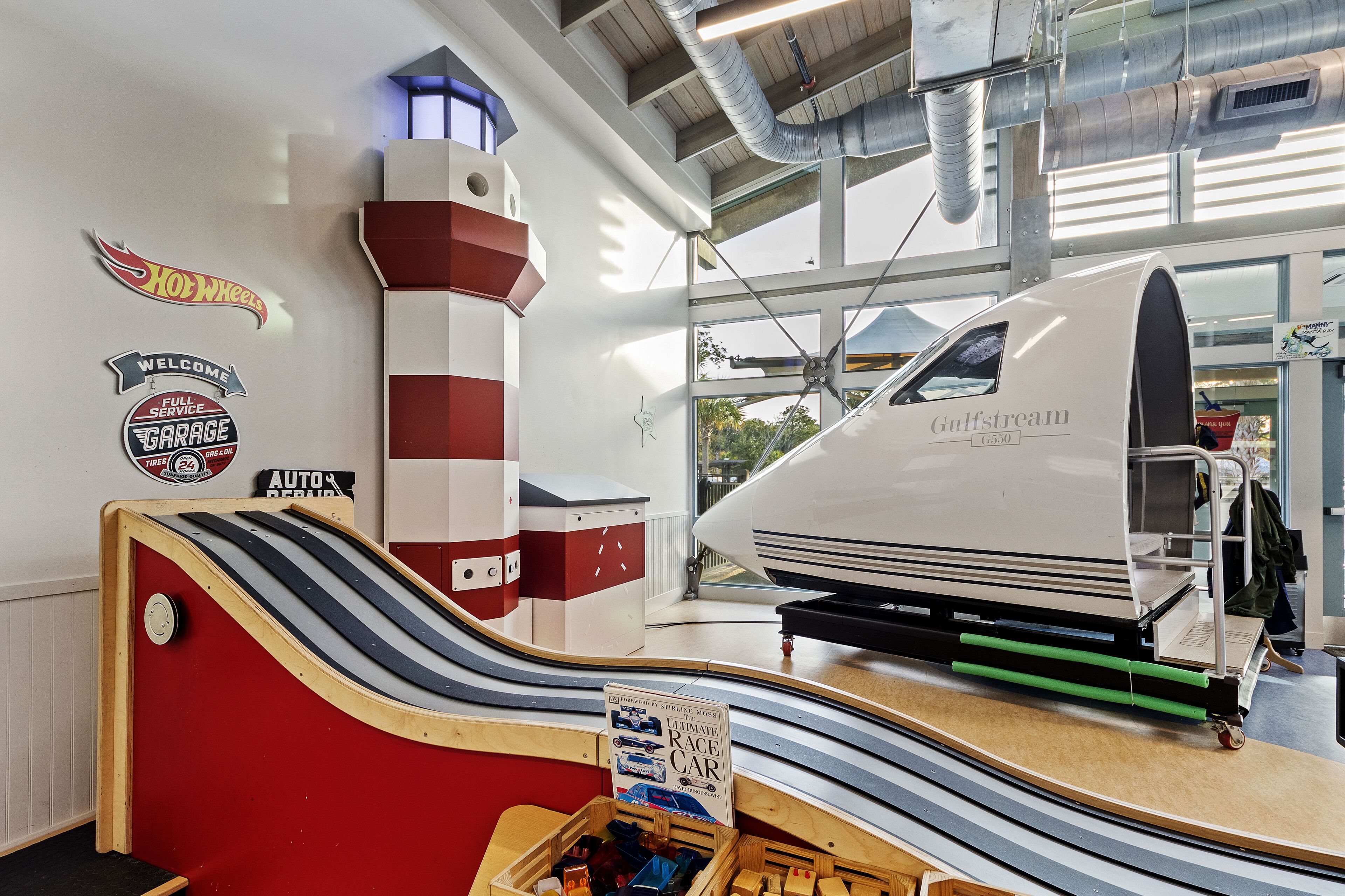 A modern indoor space with a large vehicle display, a red and white structure, and a sign for 'Ultimate Race Car'.