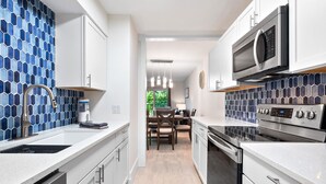 Una cucina moderna con mobili bianchi, un forno a microonde in acciaio inossidabile e un forno. Si vede anche un'area pranzo con un tavolo e sedie sullo sfondo.