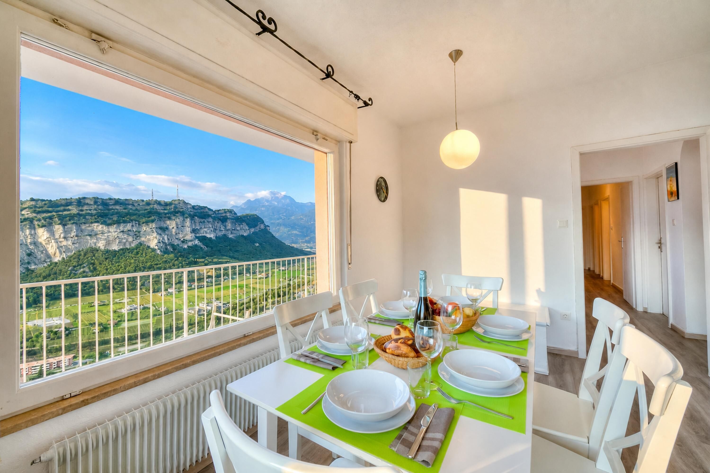 A dining area with a table set for four, a view of mountains, and a balcony with a railing.