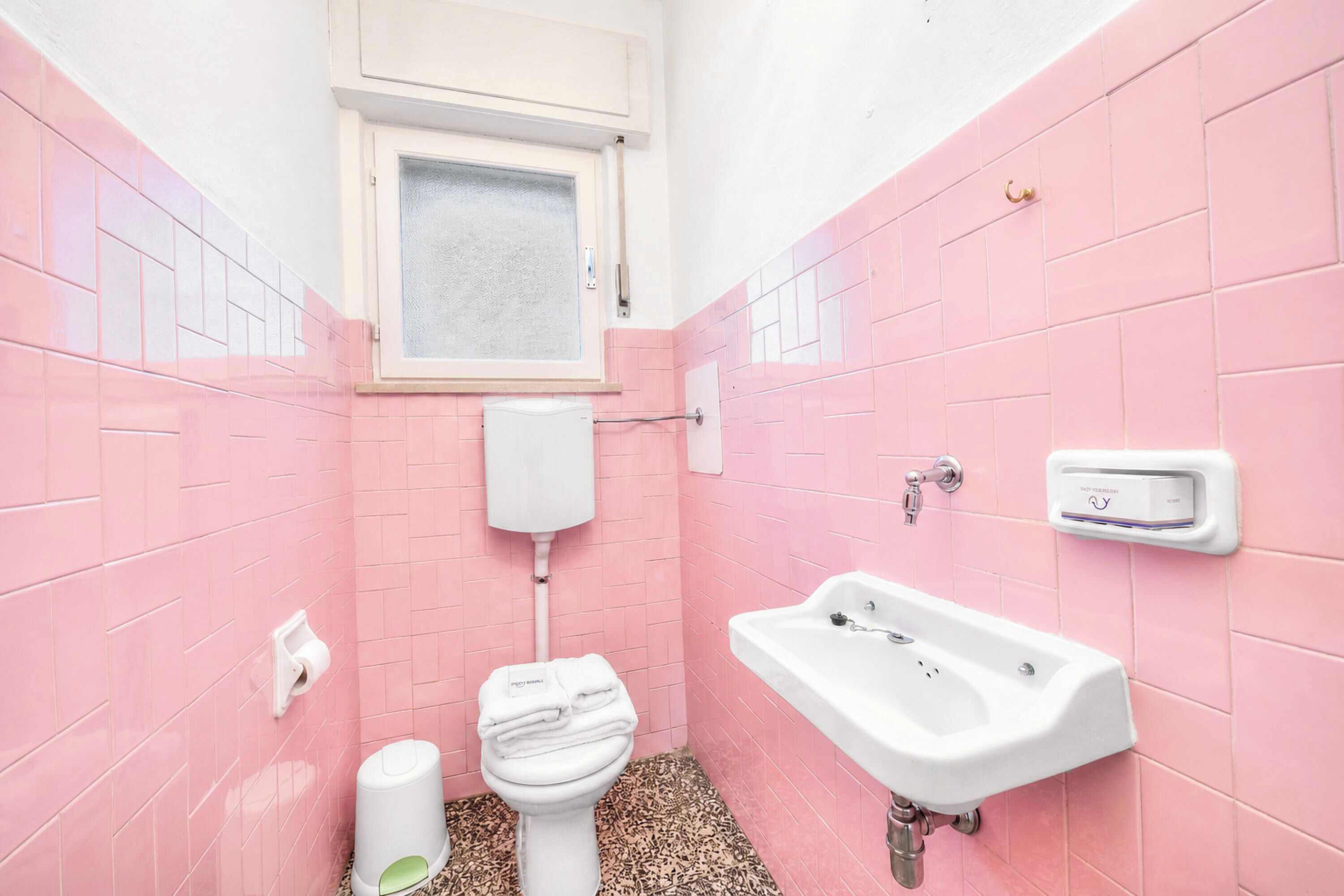 A bathroom with pink tiles, a toilet, a sink, and a window.