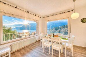 Un coin repas avec une table dressée pour quatre personnes, de grandes fenêtres offrant une vue sur les montagnes et l’eau, et un plafond blanc agrémenté d’un luminaire.