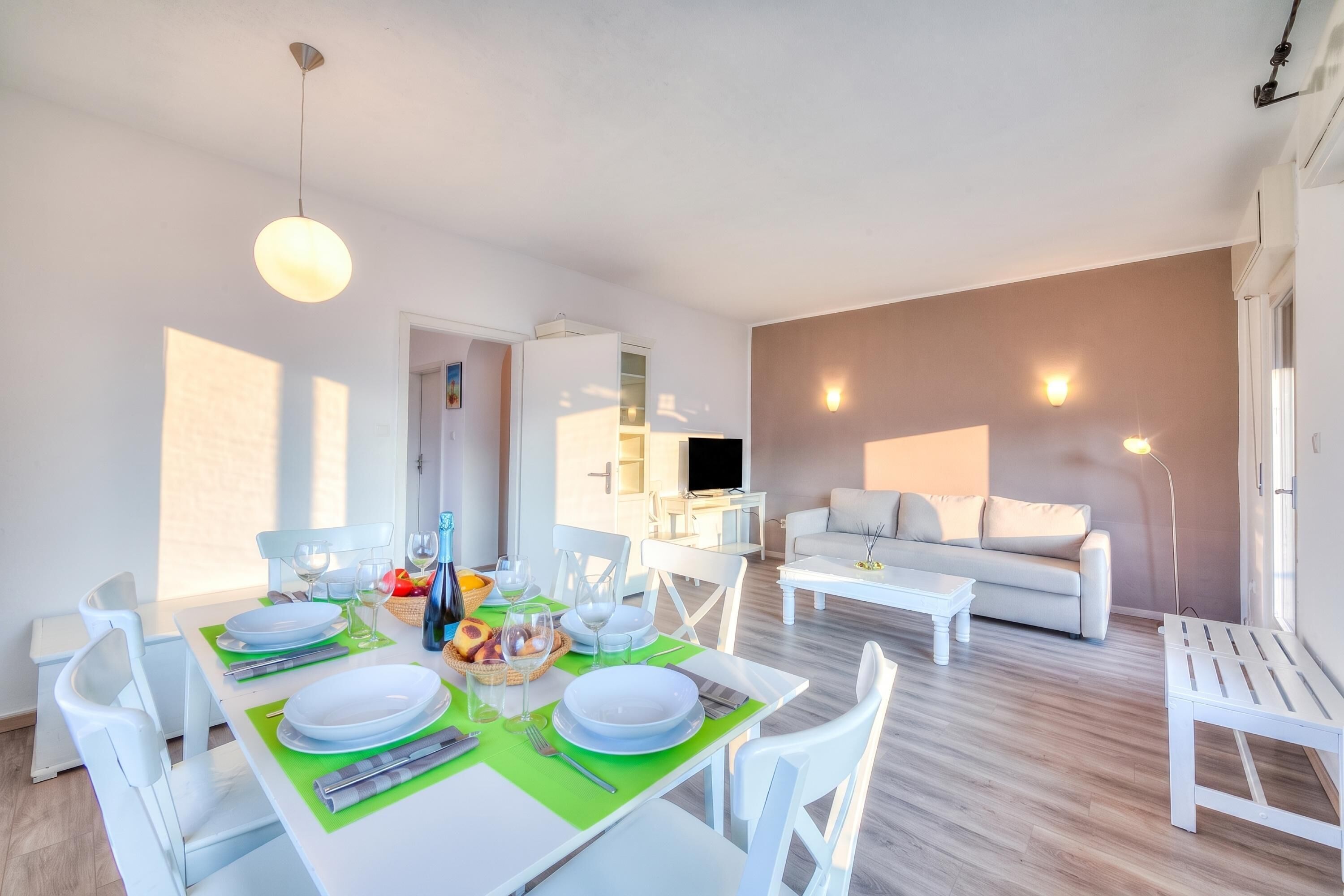 Una sala de estar moderna con comedor, muebles blancos y un televisor de pantalla plana.