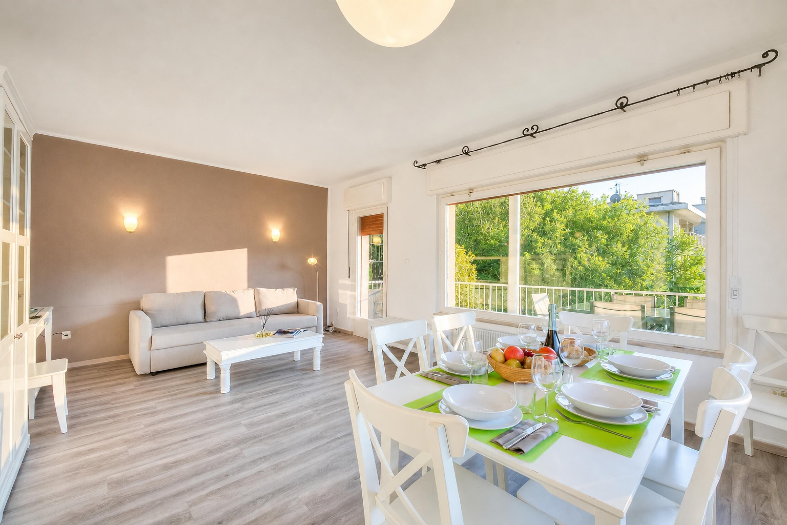 Un salon moderne comprenant un coin repas, des meubles blancs et de grandes fenêtres donnant sur un paysage verdoyant.