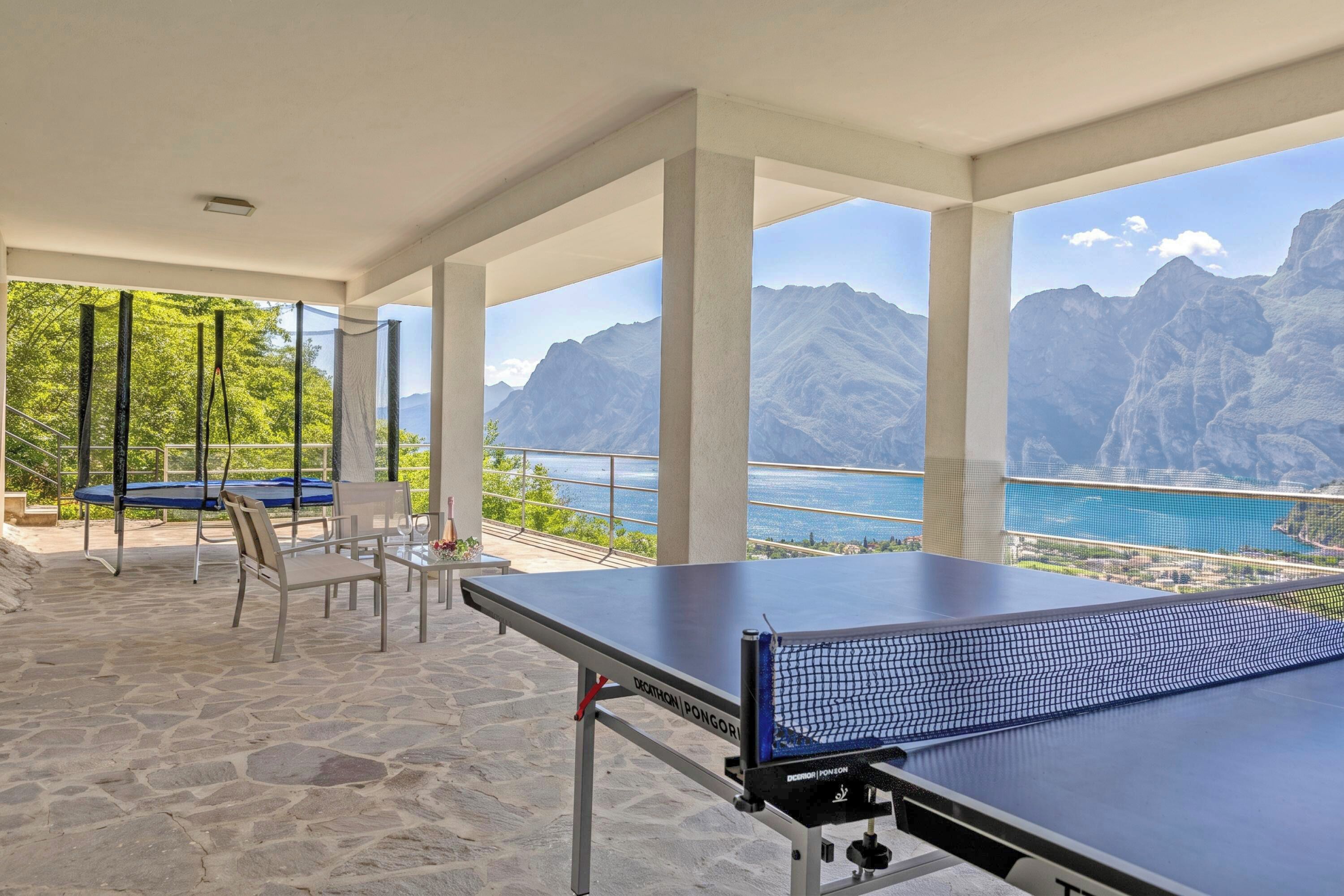 A ping pong table with a net, chairs, and a view of mountains and a lake.