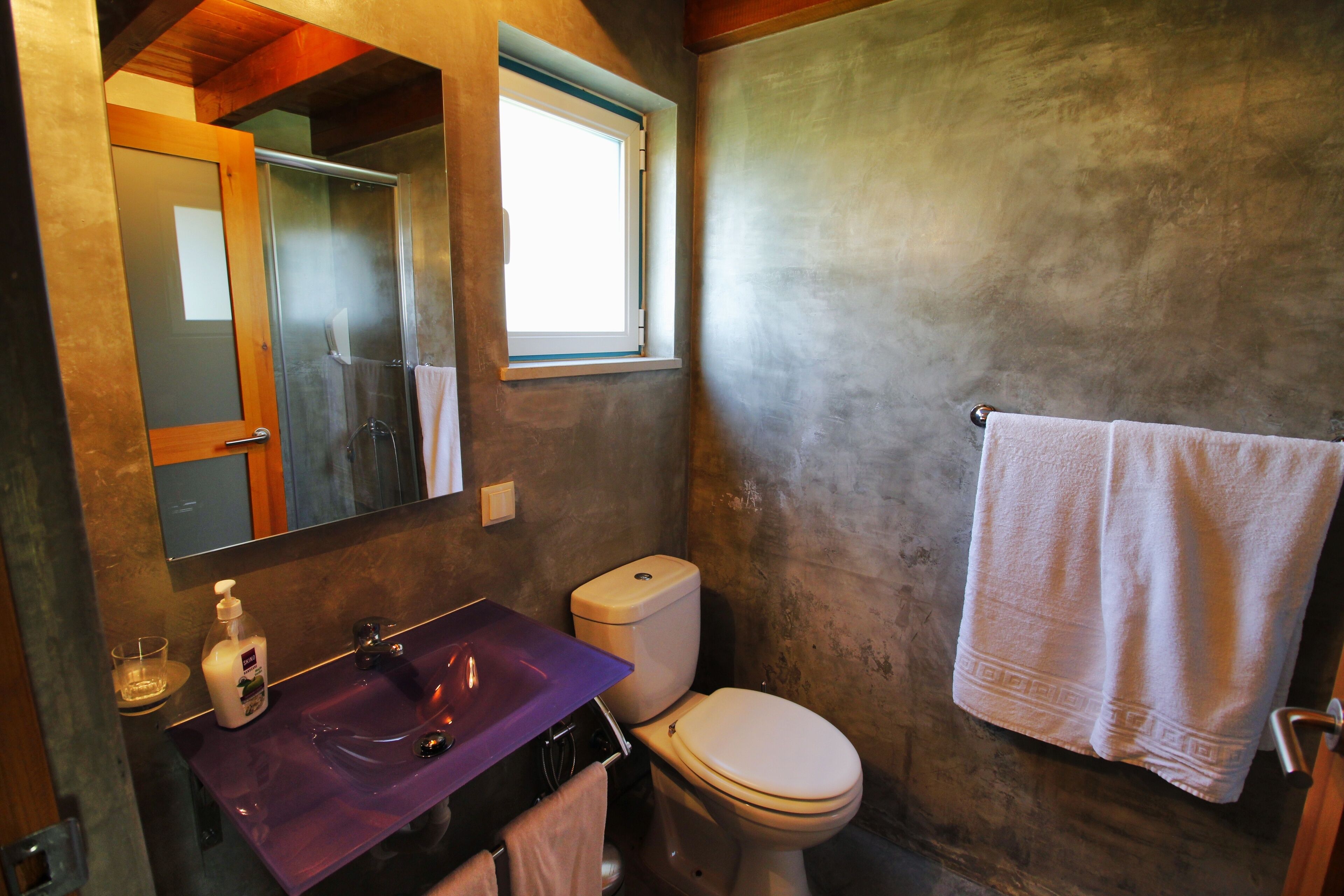 A bathroom with a purple sink, a white toilet, and a towel hanging on the wall.