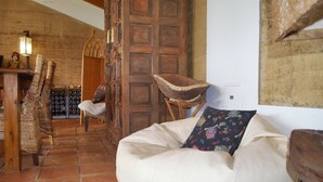 A cozy room with a stone-tiled floor, a wooden door, wicker furniture, and a white bean bag with a colorful pillow.