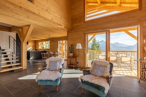 A spacious wooden interior with a staircase, a dining area, and a balcony with a mountain view.