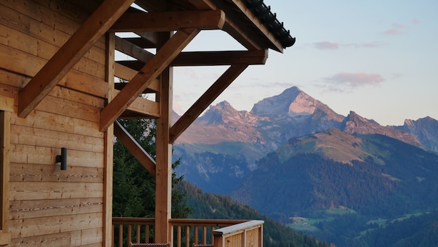 Een houten chalet met balkon, met uitzicht op een bergachtig landschap.