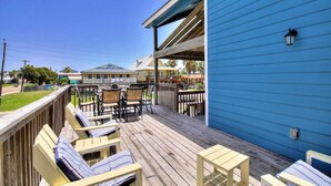 Een houten terras met lounge stoelen en een tafel, een blauw gebouw en een heldere lucht.