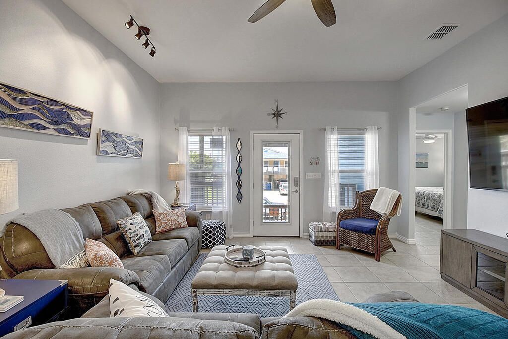 A living room with a sofa, ottoman, and chair, a television, and a door leading outside.