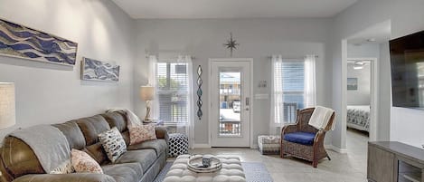 A living room with a sofa, ottoman, and chair, a television, and a door leading outside.