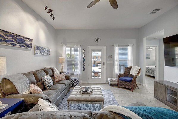 A living room with a sofa, ottoman, and chair, a television, and a door leading outside.