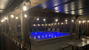 Een zwembad met blauw licht, omringd door houten stoelen en een houten hek.