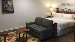A bedroom with a bed, a gray sofa, a small table, and a chair. - Eufaula House (Eufaula)