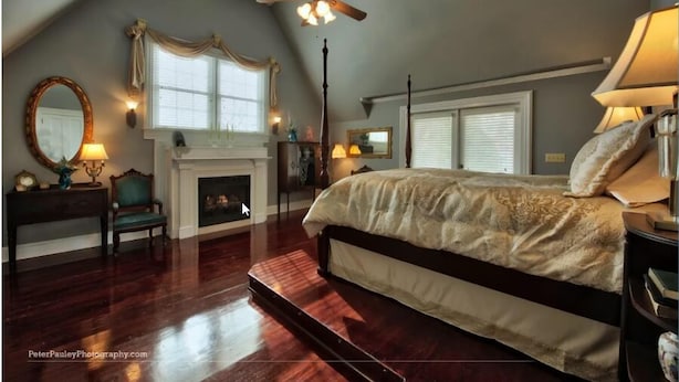 A bedroom with a large bed, a fireplace, a ceiling fan, and a view of the outdoors. - Eufaula House (Eufaula)