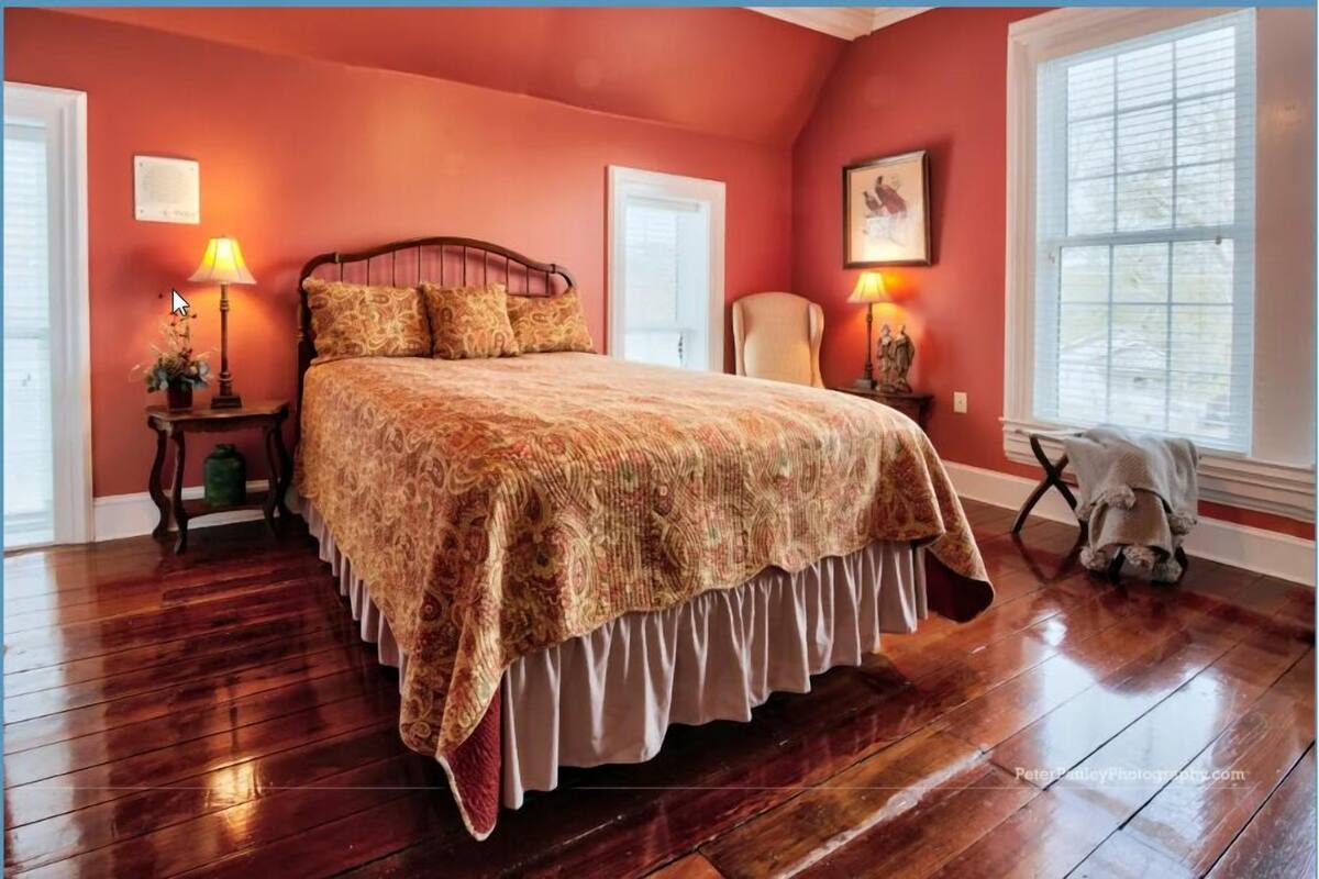 A bedroom with a large bed, two bedside tables, a chair, and a window.