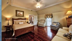 A spacious bedroom with a large bed, a sitting area with a chair, and a wooden dresser. - Eufaula House (Eufaula)