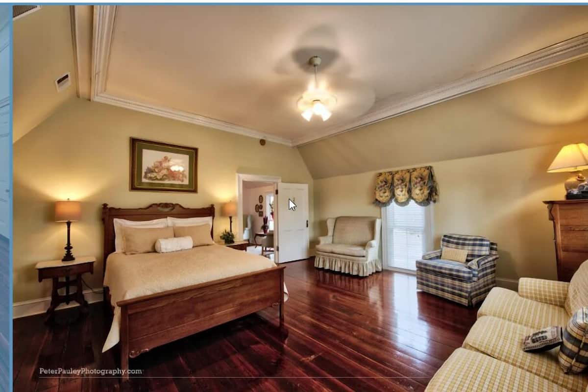 A spacious bedroom with a large bed, a sitting area with a chair, and a wooden dresser.
