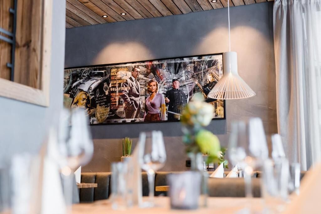 A restaurant interior with a modern design, featuring a large wall mural, wooden ceiling, and contemporary lighting fixtures.
