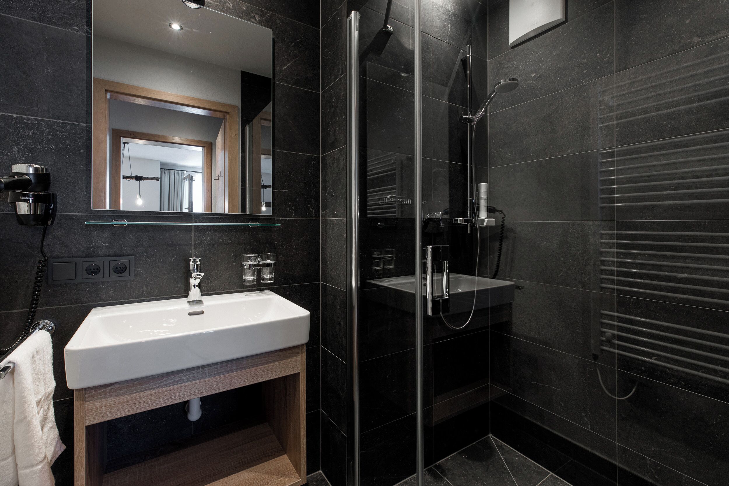 A modern bathroom with a glass shower enclosure, a white sink, and a mirror.