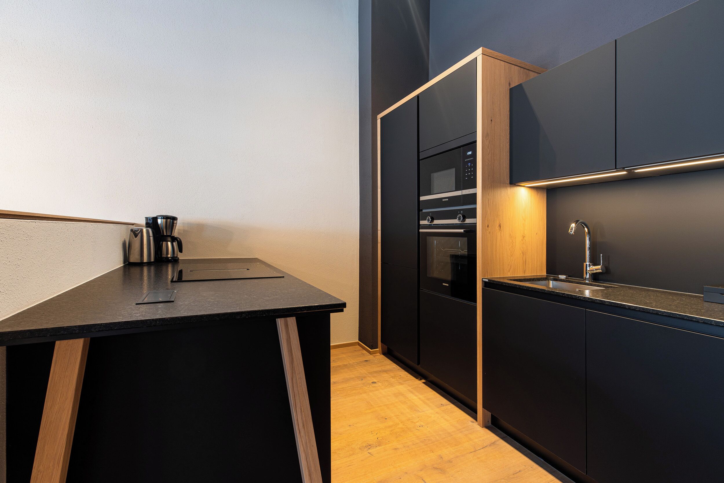 Une cuisine moderne avec des meubles de couleur sombre, un plan de travail en bois et un four encastré.