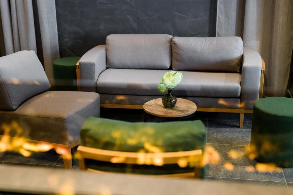 A modern living room with a grey sofa, a green ottoman, and a round wooden coffee table with a vase of flowers.