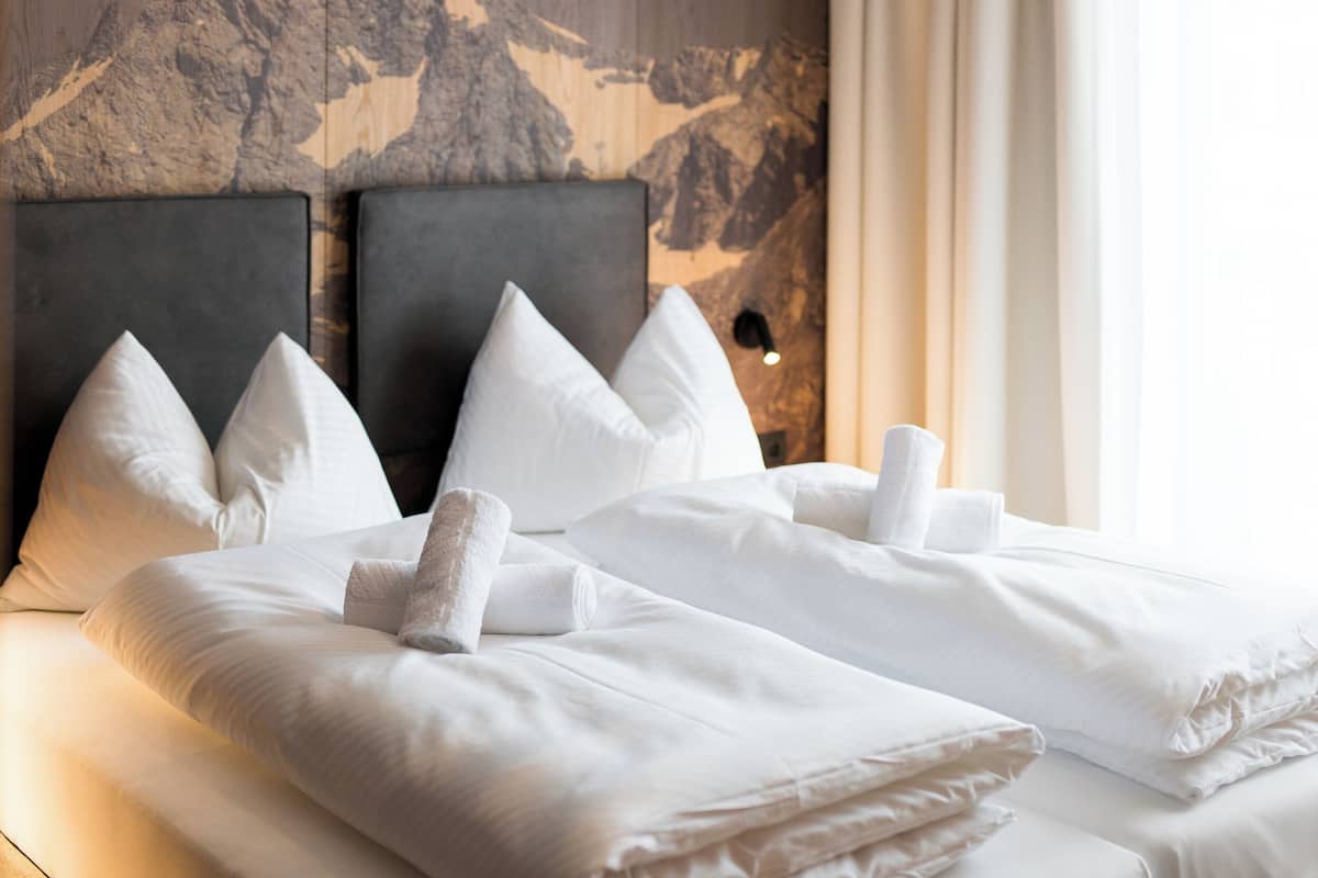 Een hotelkamer met een hoofdeinde met bergmotief, keurig opgemaakte bedden met witte lakens en een zichtbare lichtschakelaar aan de muur.