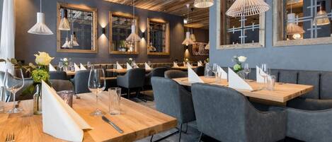 A restaurant interior with wooden tables, grey upholstered chairs, and pendant lighting.