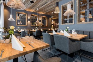 A restaurant interior with wooden tables, grey upholstered chairs, and pendant lighting.