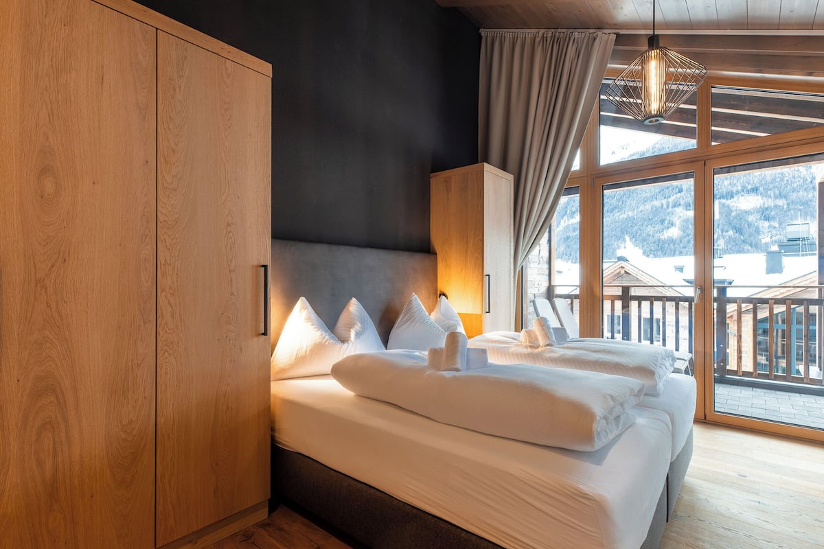 Een hotelkamer met een groot bed, een houten kledingkast en uitzicht op de bergen door het raam.