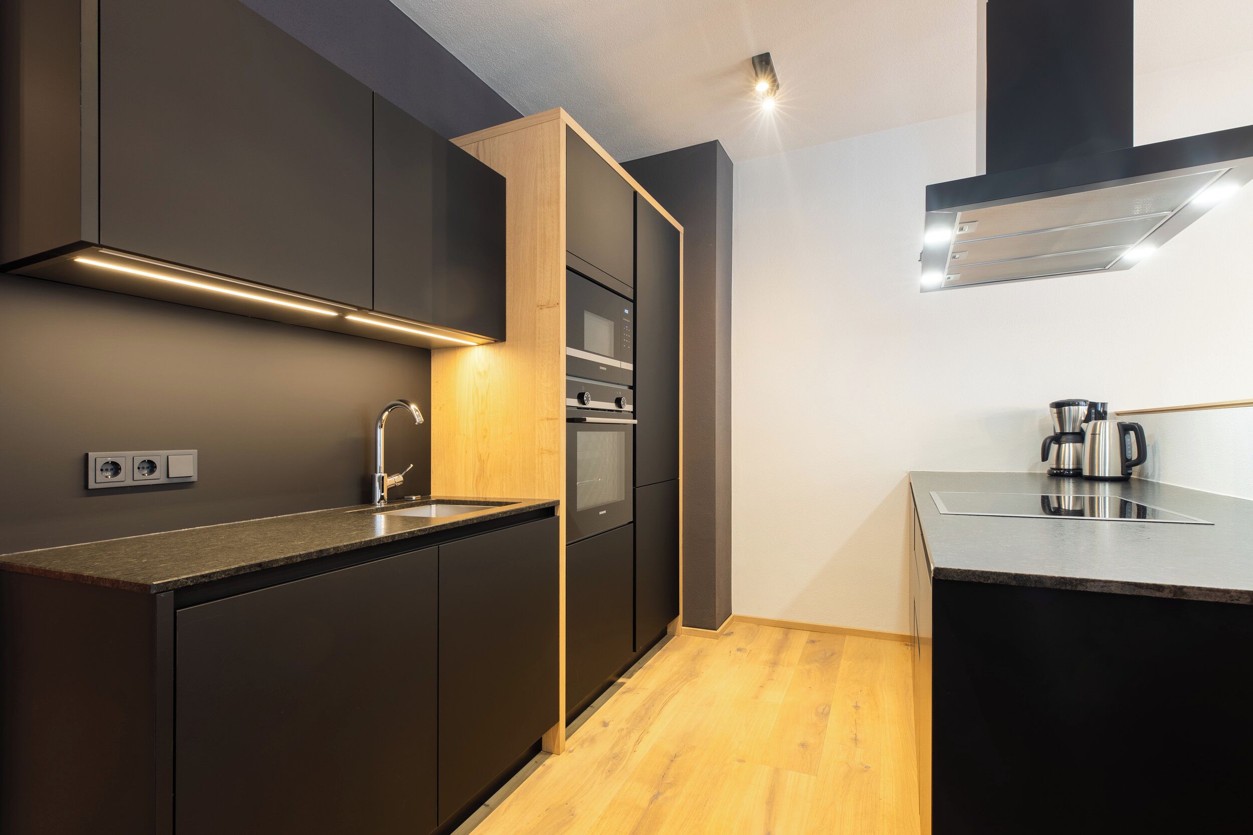 A modern kitchen with dark cabinetry, a wooden countertop, and a built-in oven.