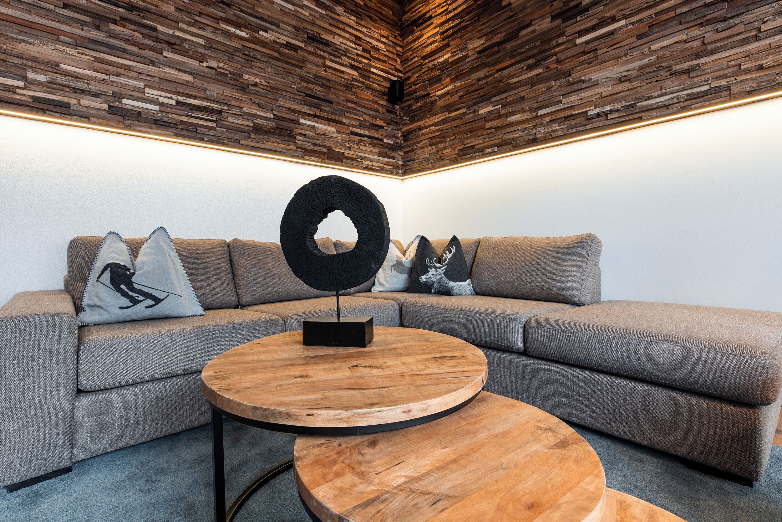 Een moderne woonkamer met een hoekbank, een ronde houten salontafel en een bijzondere ronde wanddecoratie.