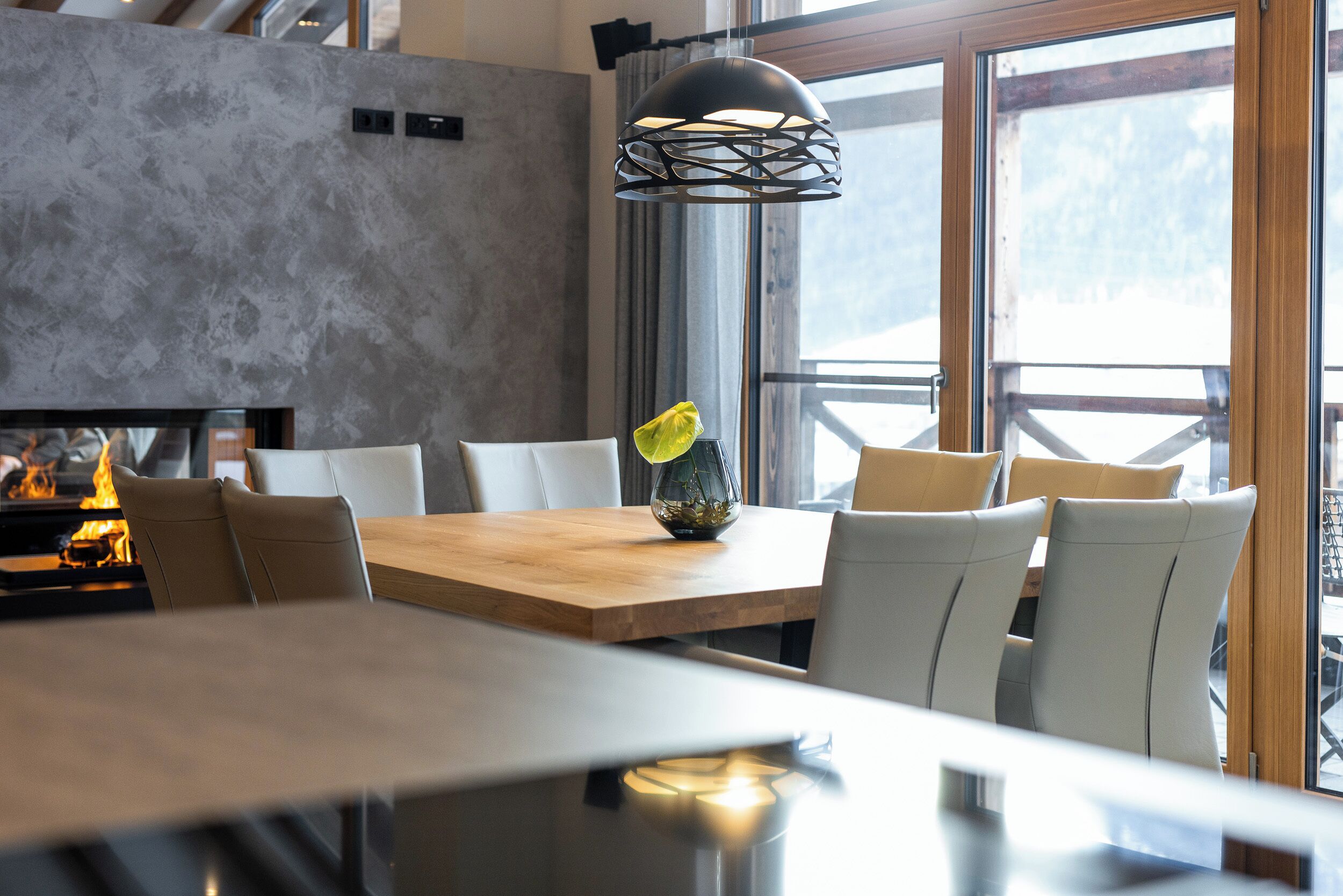 Un comedor moderno con una mesa de madera, sillas blancas y una lámpara colgante negra.