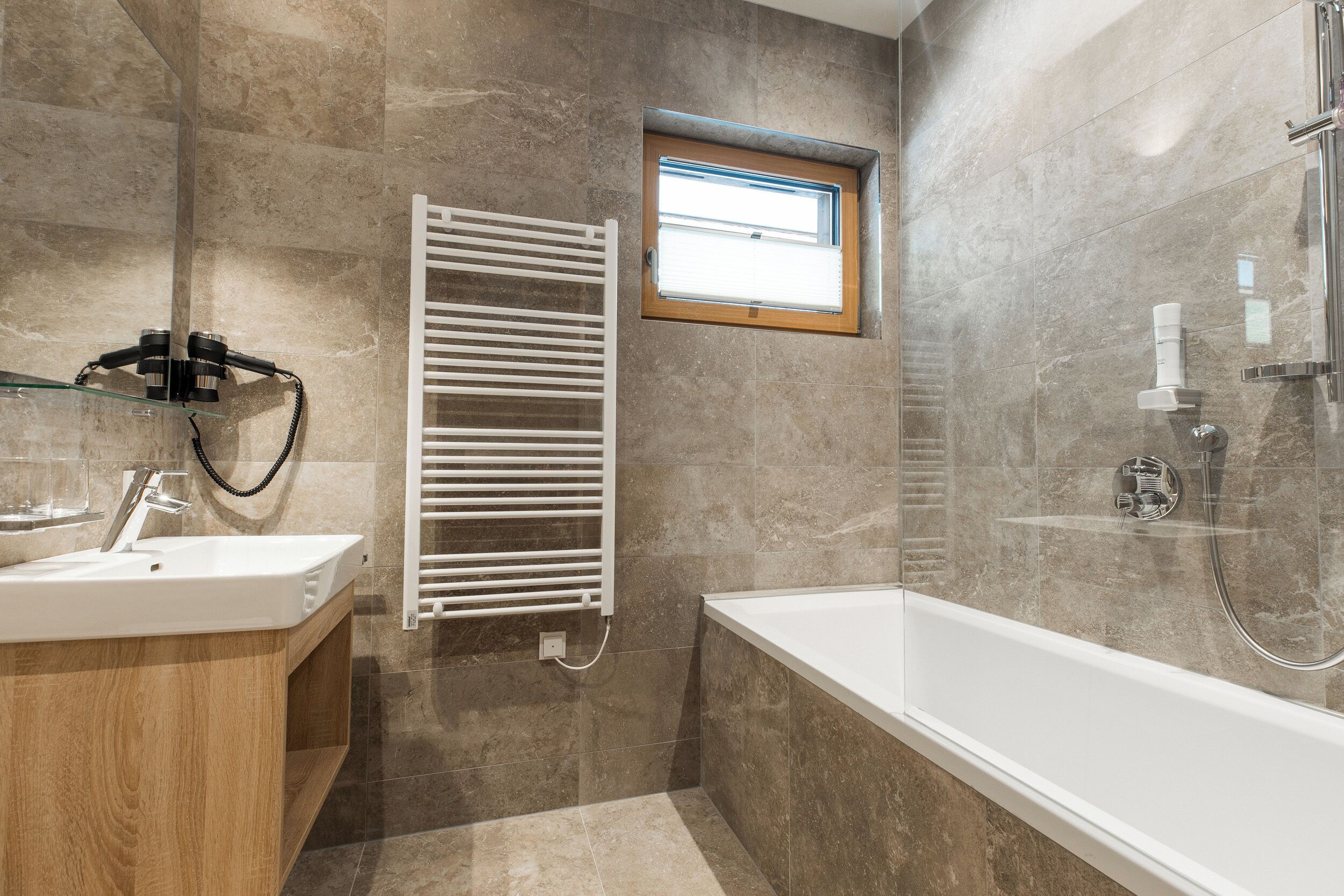 A modern bathroom with a bathtub, a glass shower enclosure, a towel rack, and a window with blinds.