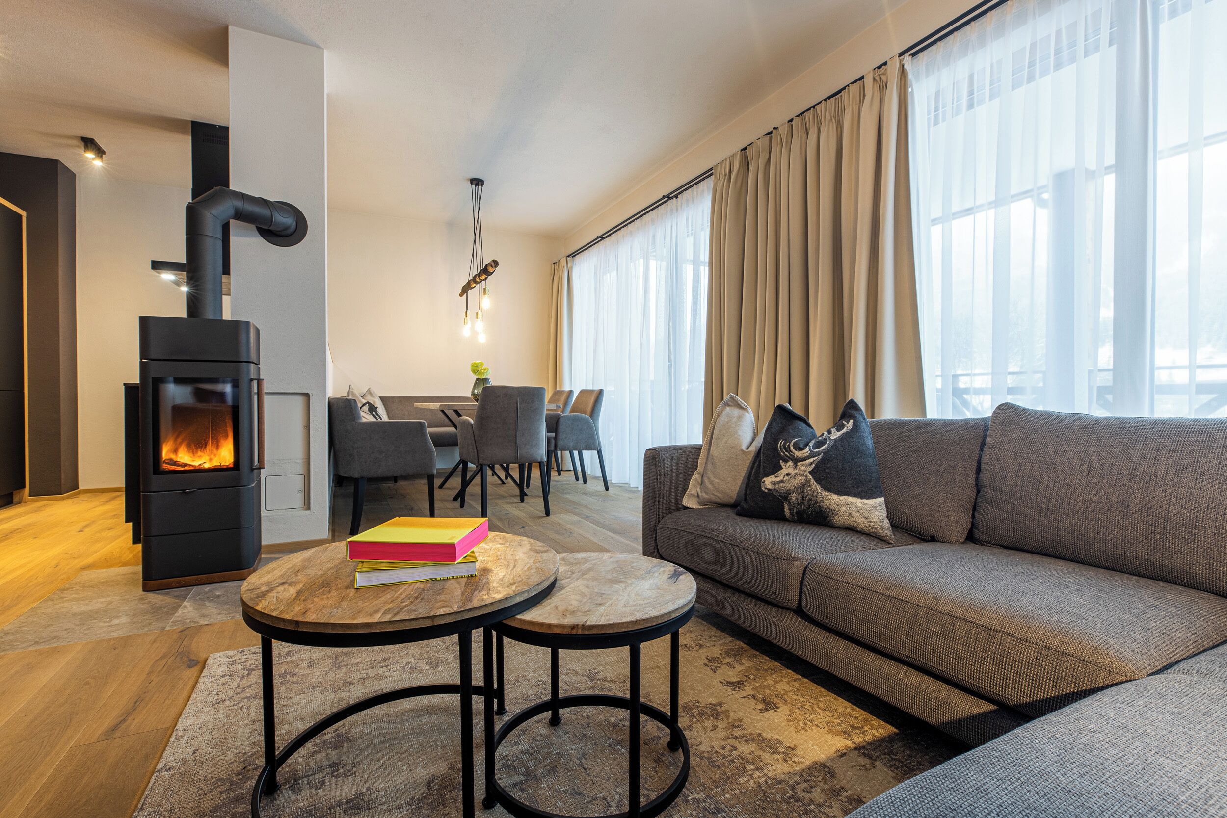 A modern living room with a wood-burning stove, a sofa, a dining area, and large windows.