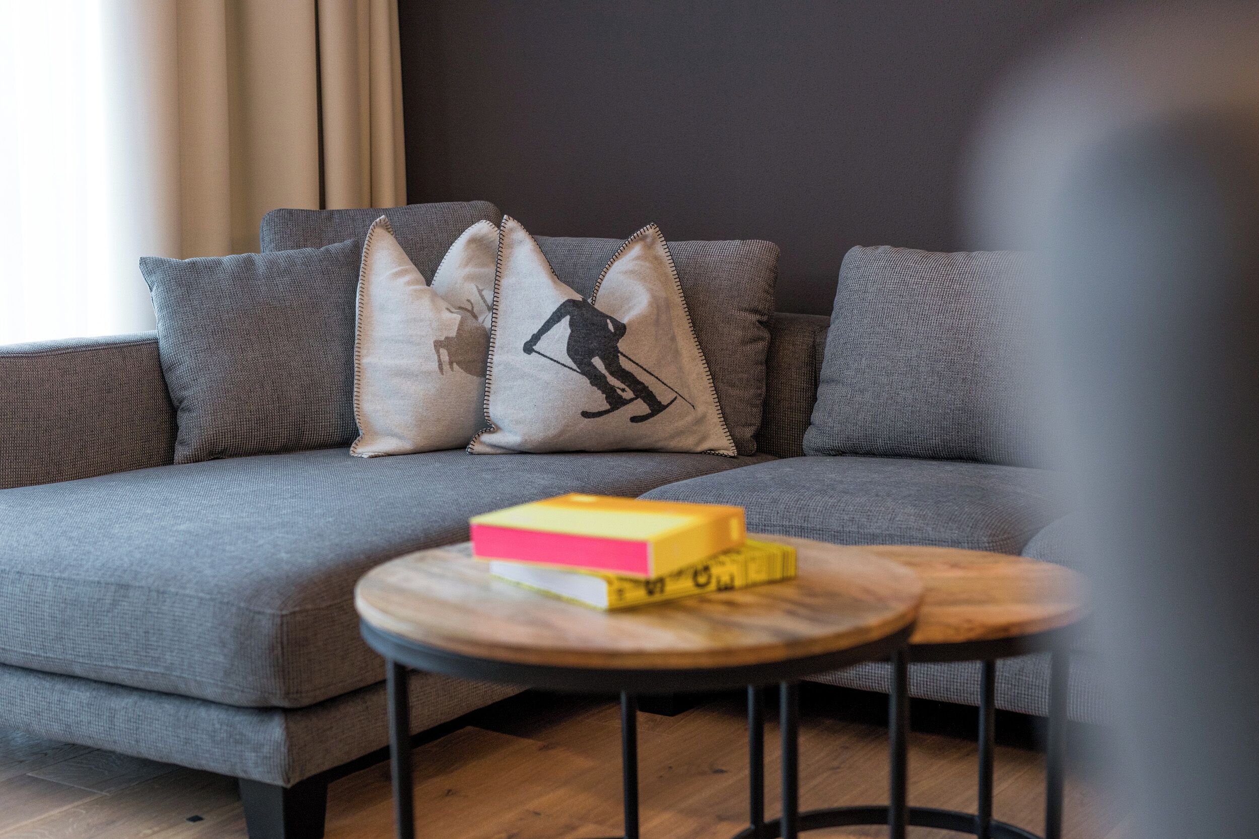 A modern living room with a grey sofa, multiple cushions, and a small wooden coffee table with books.