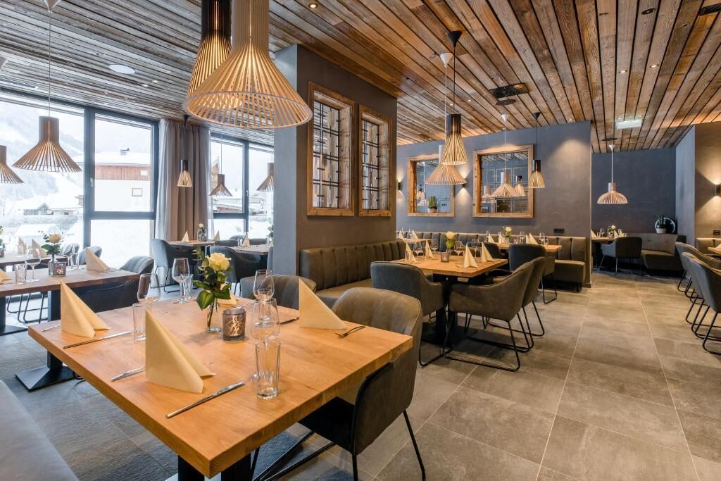 En moderne restaurant med træborde og stole, hængende lamper og store vinduer.
