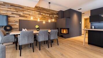 A modern dining area with a wooden wall, a fireplace, and a kitchen in the background.