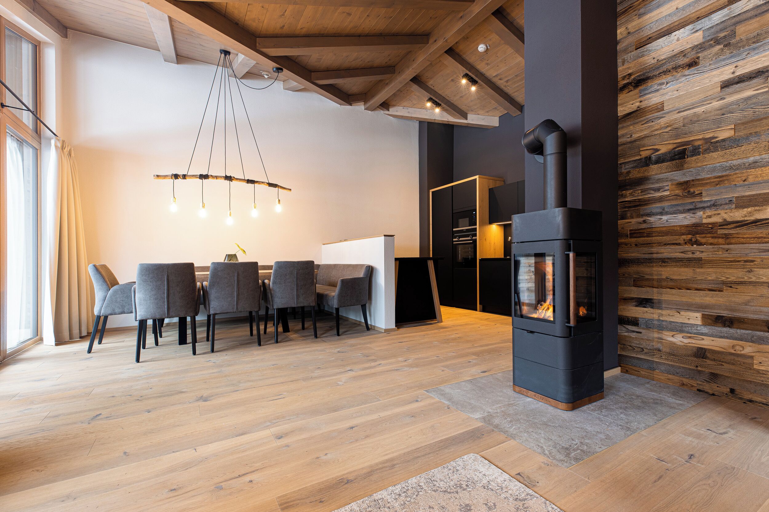 Un salon moderne comprenant un coin repas, une cheminée et des poutres apparentes.