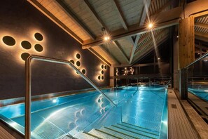 An indoor swimming pool with a glass barrier, wooden beams, and circular light fixtures on the ceiling.